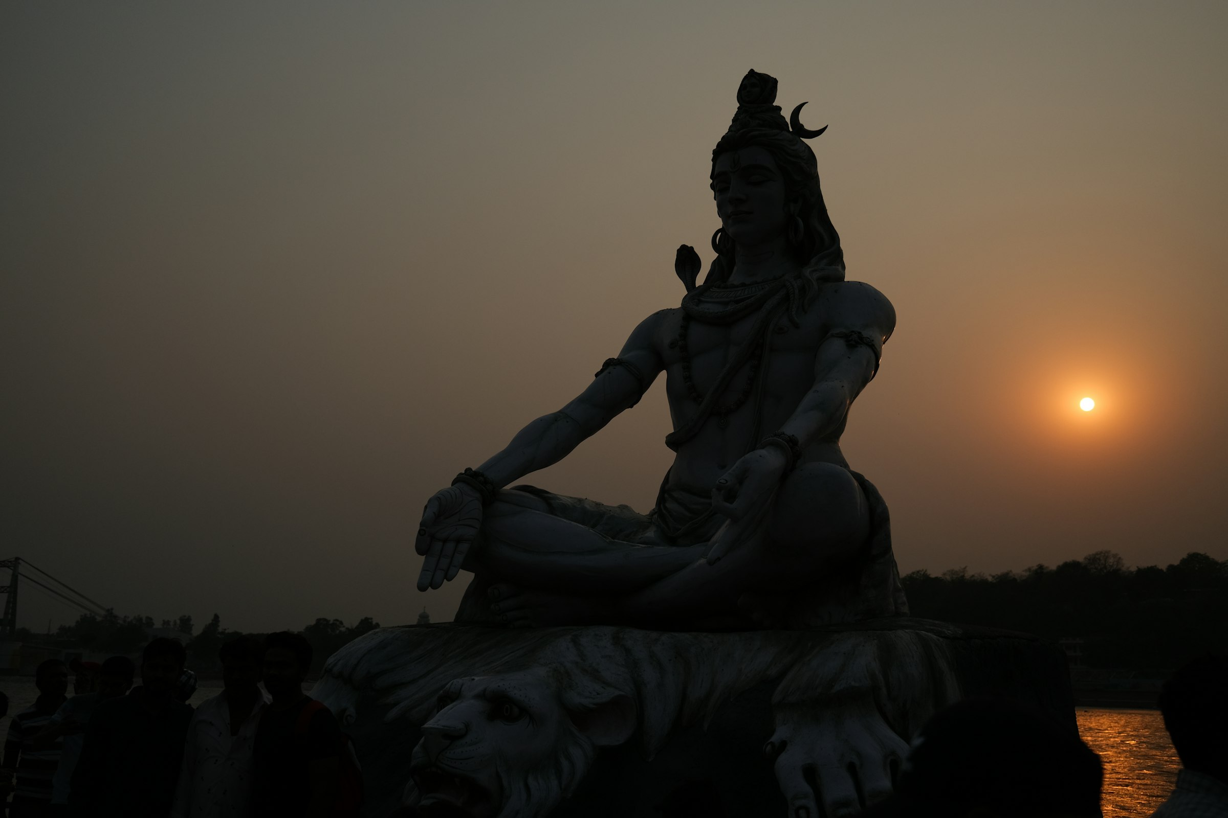 A large meditating Shiva statue against an orange sky